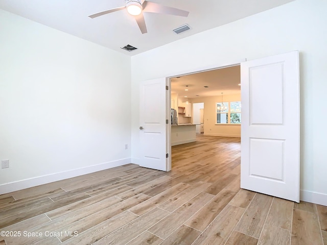 empty room with ceiling fan with notable chandelier and light hardwood / wood-style flooring