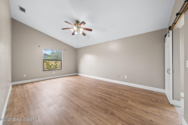 interior space featuring a textured ceiling, lofted ceiling, light wood-type flooring, ceiling fan, and a barn door