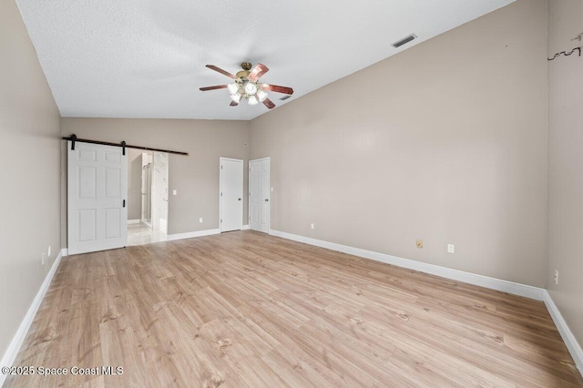 spare room with ceiling fan, a barn door, lofted ceiling, light wood-type flooring, and a textured ceiling