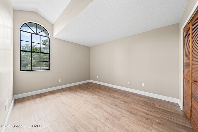 unfurnished bedroom featuring lofted ceiling, light wood-type flooring, and a closet