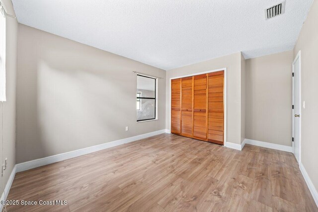 unfurnished bedroom featuring a textured ceiling, a closet, and light hardwood / wood-style flooring