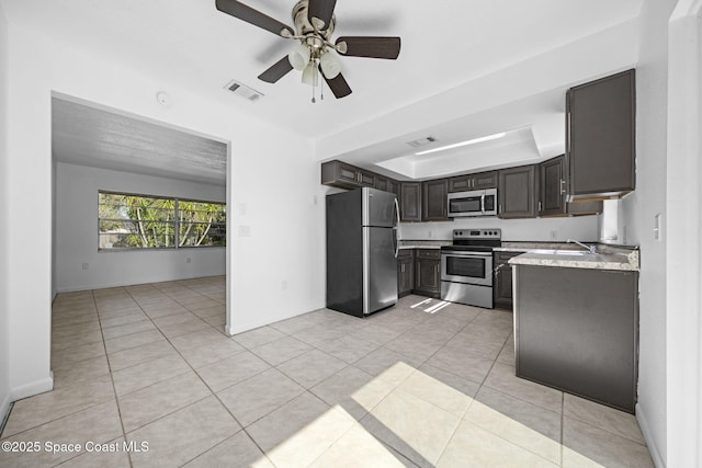 kitchen with ceiling fan, stainless steel appliances, a raised ceiling, dark brown cabinets, and light tile patterned floors