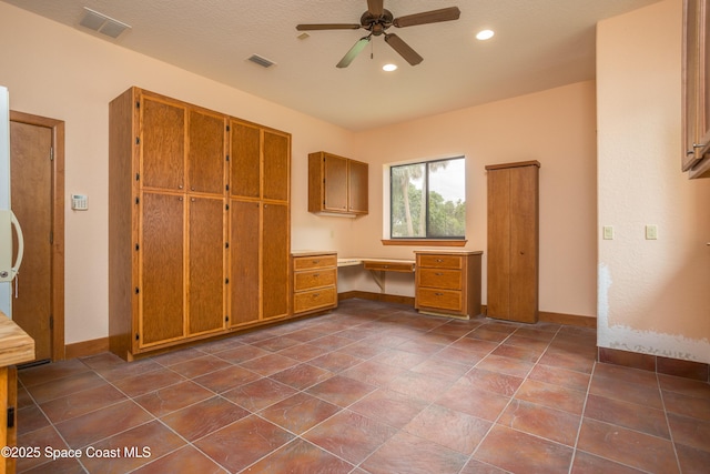 unfurnished office featuring a textured ceiling, ceiling fan, and built in desk