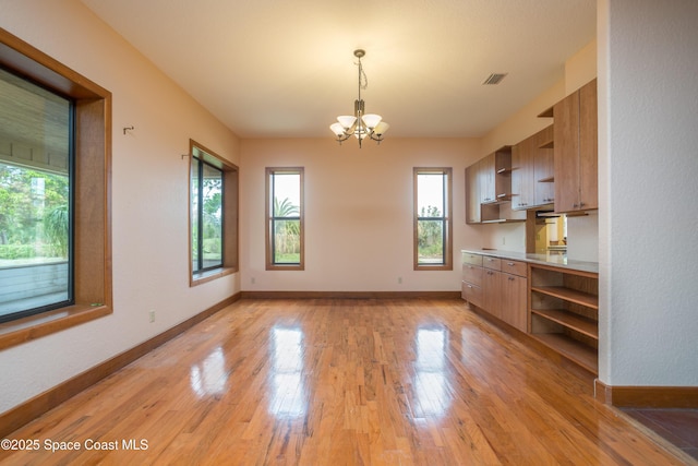 unfurnished dining area featuring an inviting chandelier and light hardwood / wood-style flooring