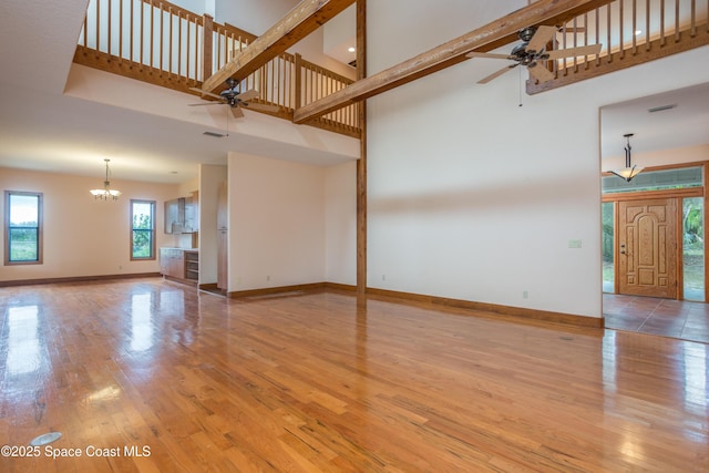 unfurnished living room featuring light hardwood / wood-style floors, a towering ceiling, and ceiling fan with notable chandelier