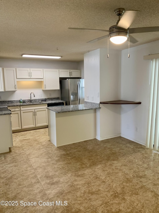 kitchen with white cabinets, sink, stainless steel fridge, dark stone countertops, and a textured ceiling