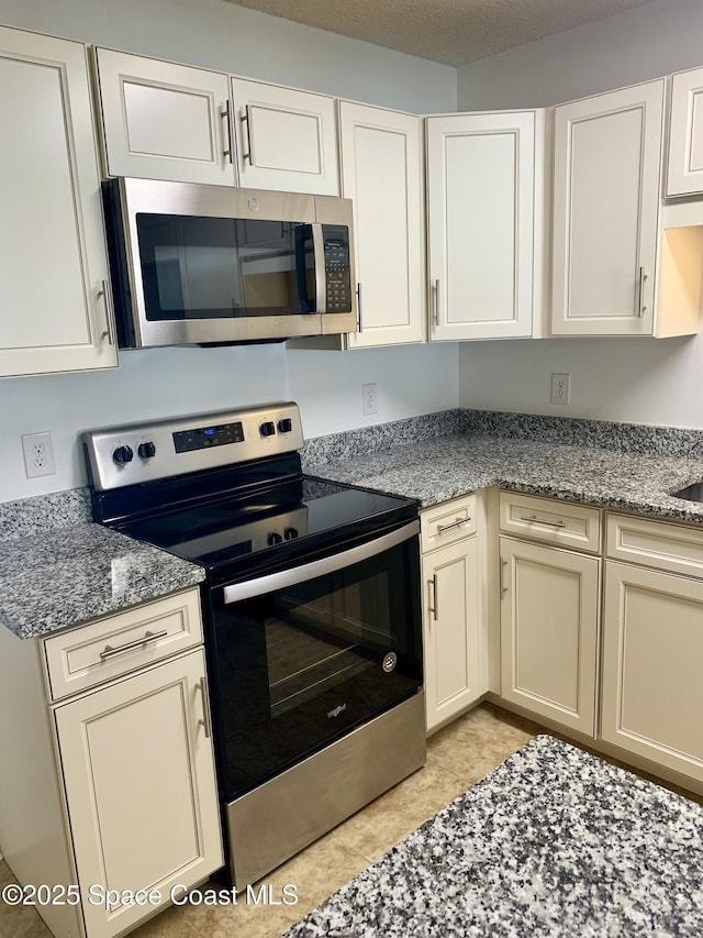 kitchen with white cabinetry, light tile patterned floors, stainless steel appliances, and stone counters