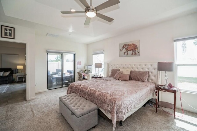 carpeted bedroom featuring ceiling fan, access to exterior, and a tray ceiling