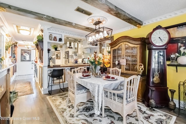 dining space with ornamental molding, light wood-type flooring, an inviting chandelier, and a textured ceiling