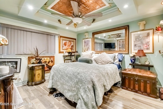 bedroom with ceiling fan, crown molding, light wood-type flooring, and a raised ceiling