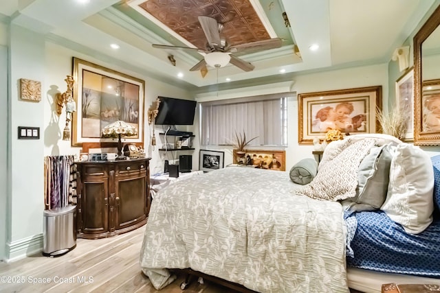 bedroom with a raised ceiling, ceiling fan, ornamental molding, and light hardwood / wood-style flooring