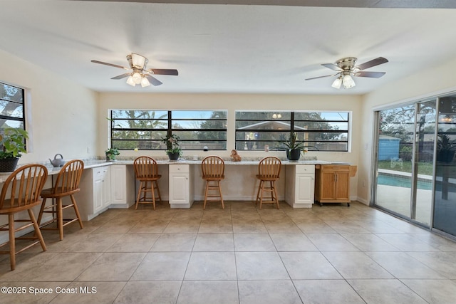 kitchen featuring light stone counters, a breakfast bar, white cabinets, and ceiling fan