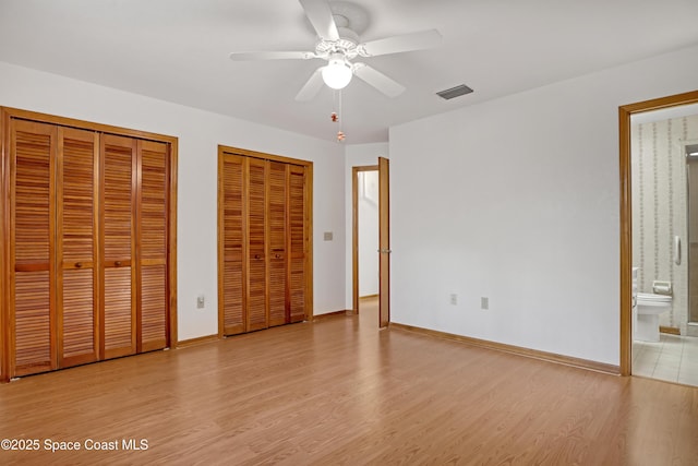 unfurnished bedroom featuring ceiling fan, multiple closets, connected bathroom, and light hardwood / wood-style flooring