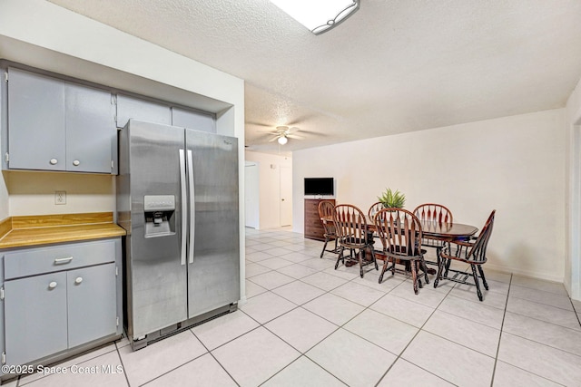 kitchen featuring a textured ceiling, light tile patterned floors, gray cabinetry, ceiling fan, and stainless steel fridge