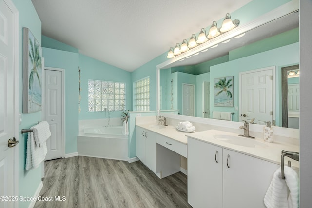 bathroom featuring hardwood / wood-style floors, vanity, lofted ceiling, a textured ceiling, and a tub