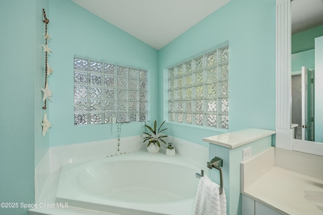 bathroom featuring tiled bath, vanity, and vaulted ceiling