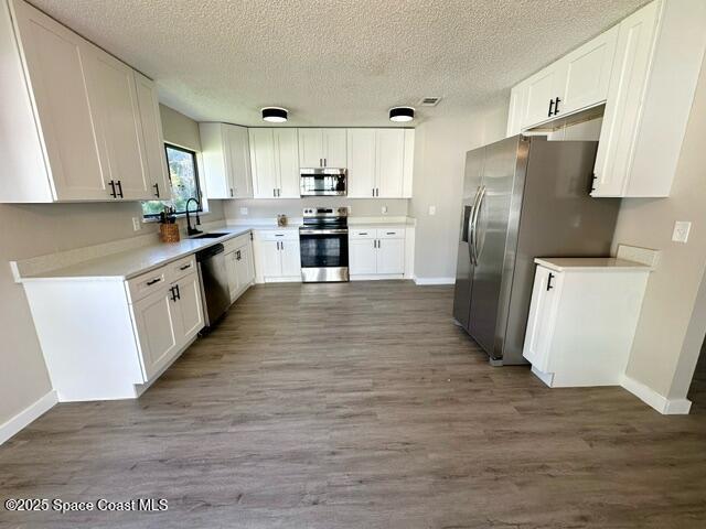 kitchen featuring white cabinets, appliances with stainless steel finishes, dark wood-type flooring, and sink