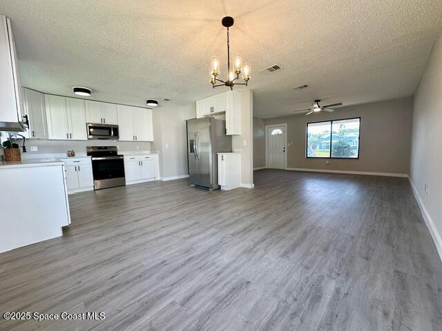 kitchen featuring white cabinets, ceiling fan with notable chandelier, hanging light fixtures, hardwood / wood-style flooring, and appliances with stainless steel finishes