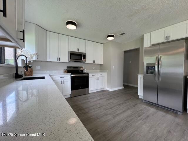 kitchen featuring sink, a textured ceiling, light stone counters, white cabinetry, and stainless steel appliances