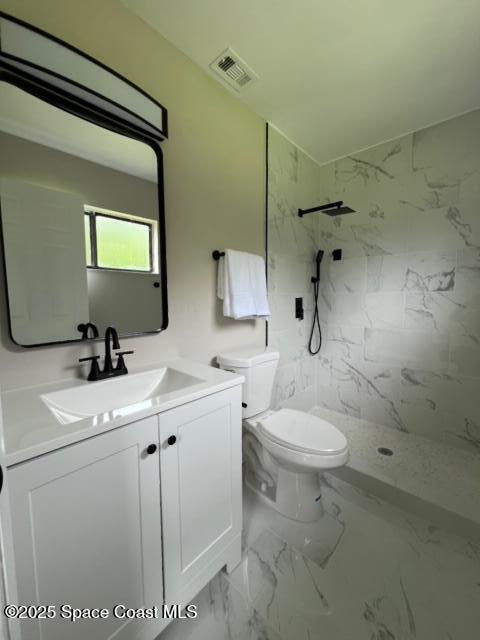 bathroom with toilet, vanity, and tiled shower