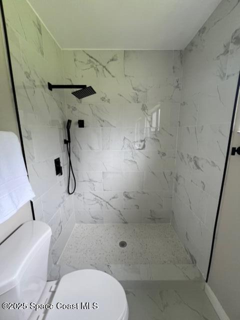 bathroom with a tile shower and toilet