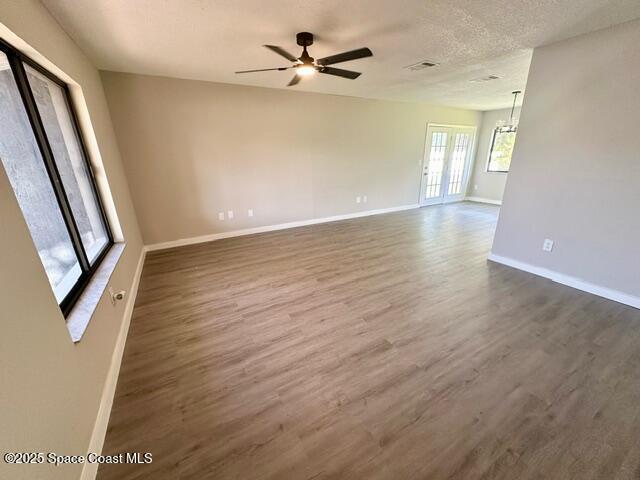 empty room with a textured ceiling, ceiling fan with notable chandelier, and dark wood-type flooring