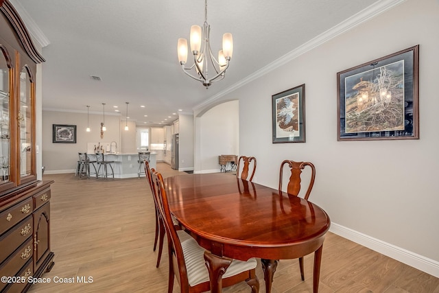 dining room with sink, light hardwood / wood-style flooring, ornamental molding, and a notable chandelier