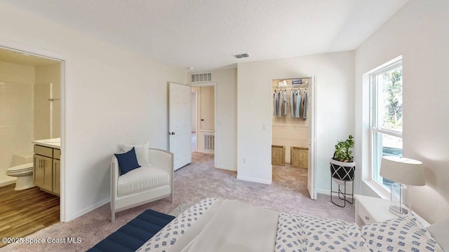 carpeted bedroom with a textured ceiling, connected bathroom, and a closet