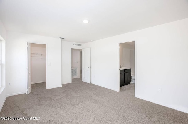 unfurnished bedroom with light carpet, ensuite bathroom, a spacious closet, and a closet