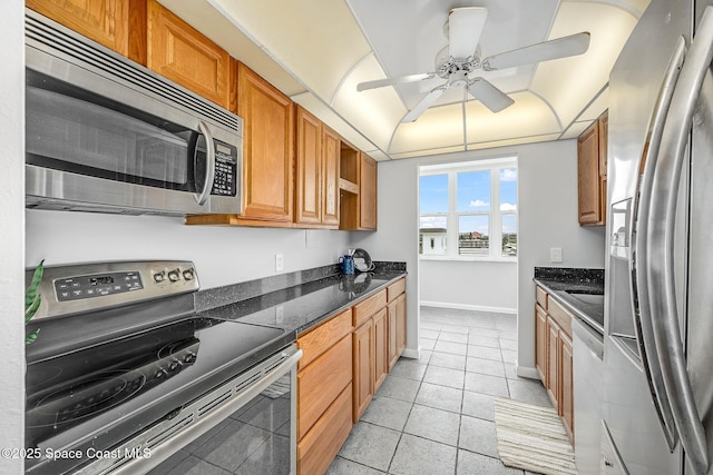 kitchen with ceiling fan, light tile patterned floors, stainless steel appliances, and dark stone counters