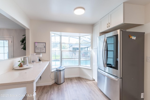 kitchen featuring kitchen peninsula, stainless steel fridge, light wood-type flooring, white cabinets, and light stone counters