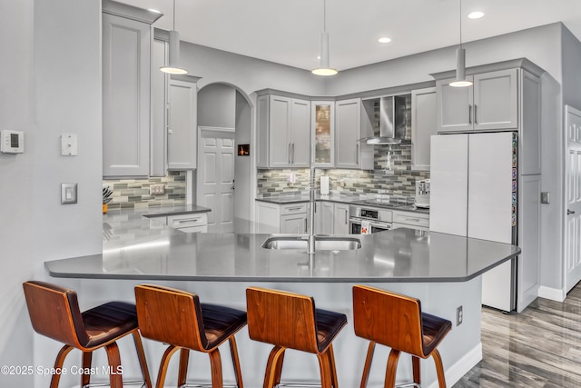 kitchen featuring kitchen peninsula, hanging light fixtures, wall chimney exhaust hood, and a breakfast bar area