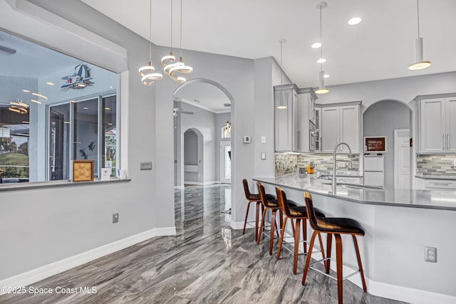 kitchen with backsplash, gray cabinetry, sink, pendant lighting, and a breakfast bar area