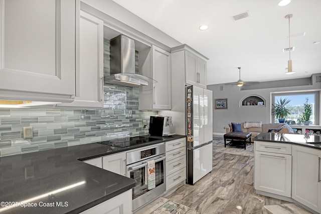 kitchen with refrigerator, wall chimney exhaust hood, black electric cooktop, oven, and hanging light fixtures