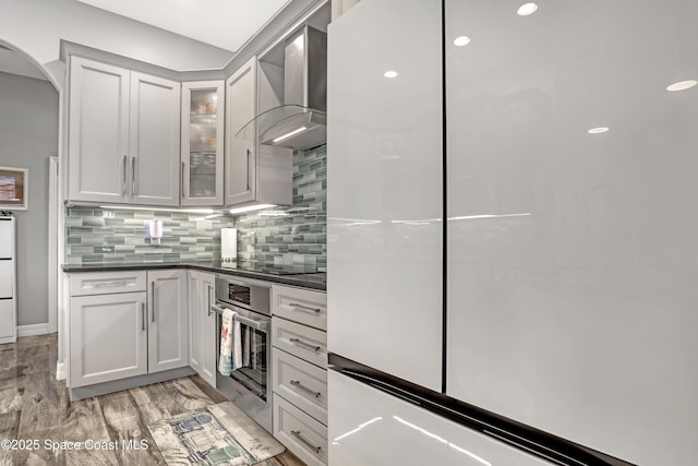 kitchen with white cabinetry, stainless steel oven, wall chimney range hood, and black electric stovetop