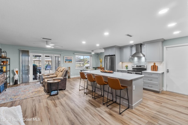 kitchen with a kitchen bar, tasteful backsplash, a center island, stainless steel appliances, and wall chimney range hood