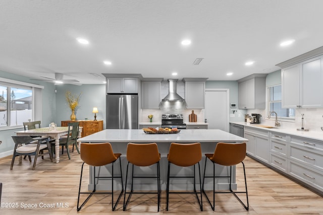 kitchen featuring stainless steel appliances, a center island, sink, and wall chimney exhaust hood