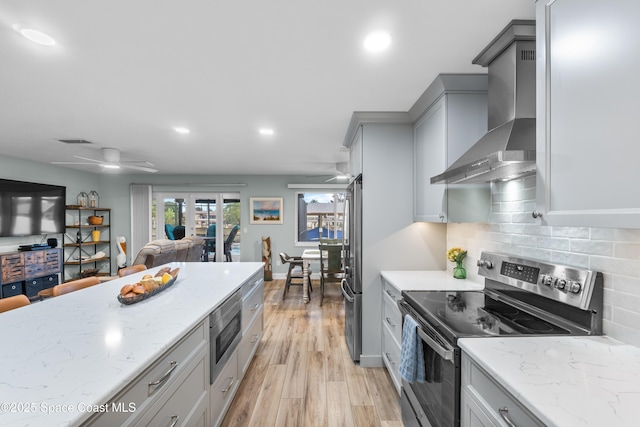 kitchen featuring wall chimney range hood, gray cabinets, ceiling fan, stainless steel appliances, and decorative backsplash