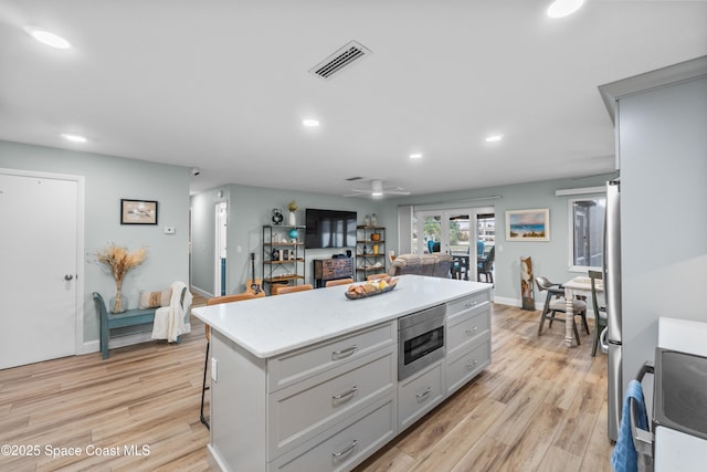 kitchen with a kitchen island, appliances with stainless steel finishes, a breakfast bar area, ceiling fan, and light hardwood / wood-style flooring