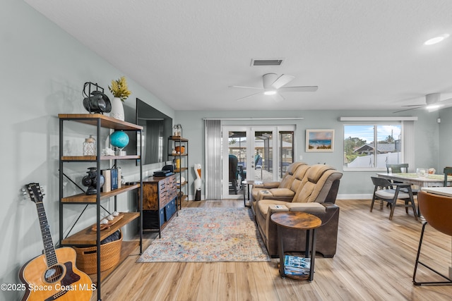 living room featuring french doors, ceiling fan, light hardwood / wood-style flooring, and a textured ceiling