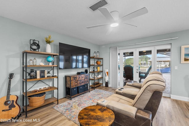 living room with ceiling fan, a textured ceiling, light wood-type flooring, and french doors