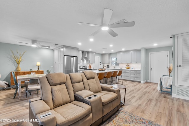 living room featuring ceiling fan, a textured ceiling, and light wood-type flooring