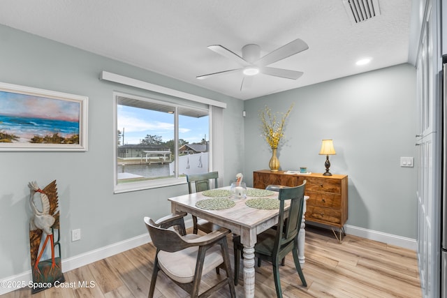 dining room with ceiling fan, a water view, a textured ceiling, and light wood-type flooring