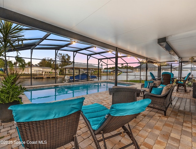 pool at dusk with an outdoor living space, a lanai, a patio area, and a water view