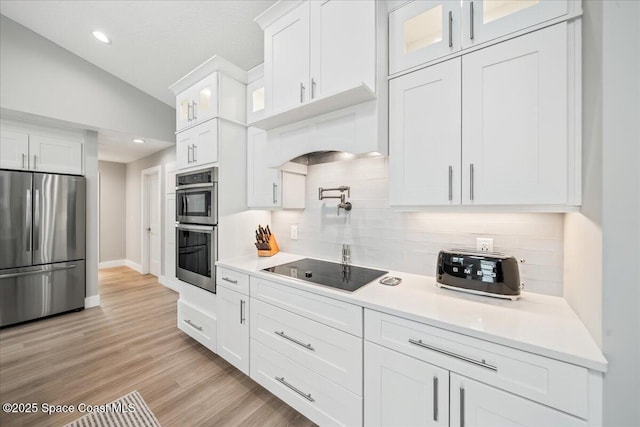 kitchen with light hardwood / wood-style floors, white cabinets, backsplash, stainless steel appliances, and lofted ceiling