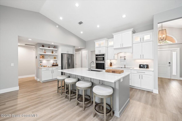 kitchen featuring white cabinets, appliances with stainless steel finishes, a kitchen bar, decorative backsplash, and a kitchen island with sink