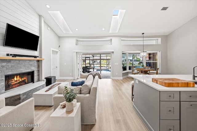 living room featuring a high ceiling, light hardwood / wood-style flooring, and a skylight