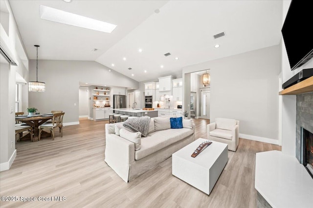 living room featuring sink, lofted ceiling with skylight, an inviting chandelier, and light wood-type flooring