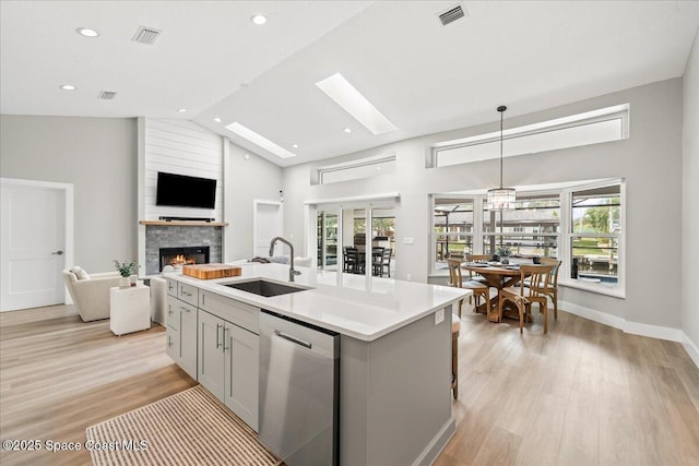 kitchen featuring decorative light fixtures, an island with sink, sink, gray cabinets, and stainless steel dishwasher