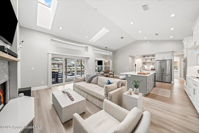 living room with sink, light hardwood / wood-style flooring, vaulted ceiling with skylight, and a brick fireplace